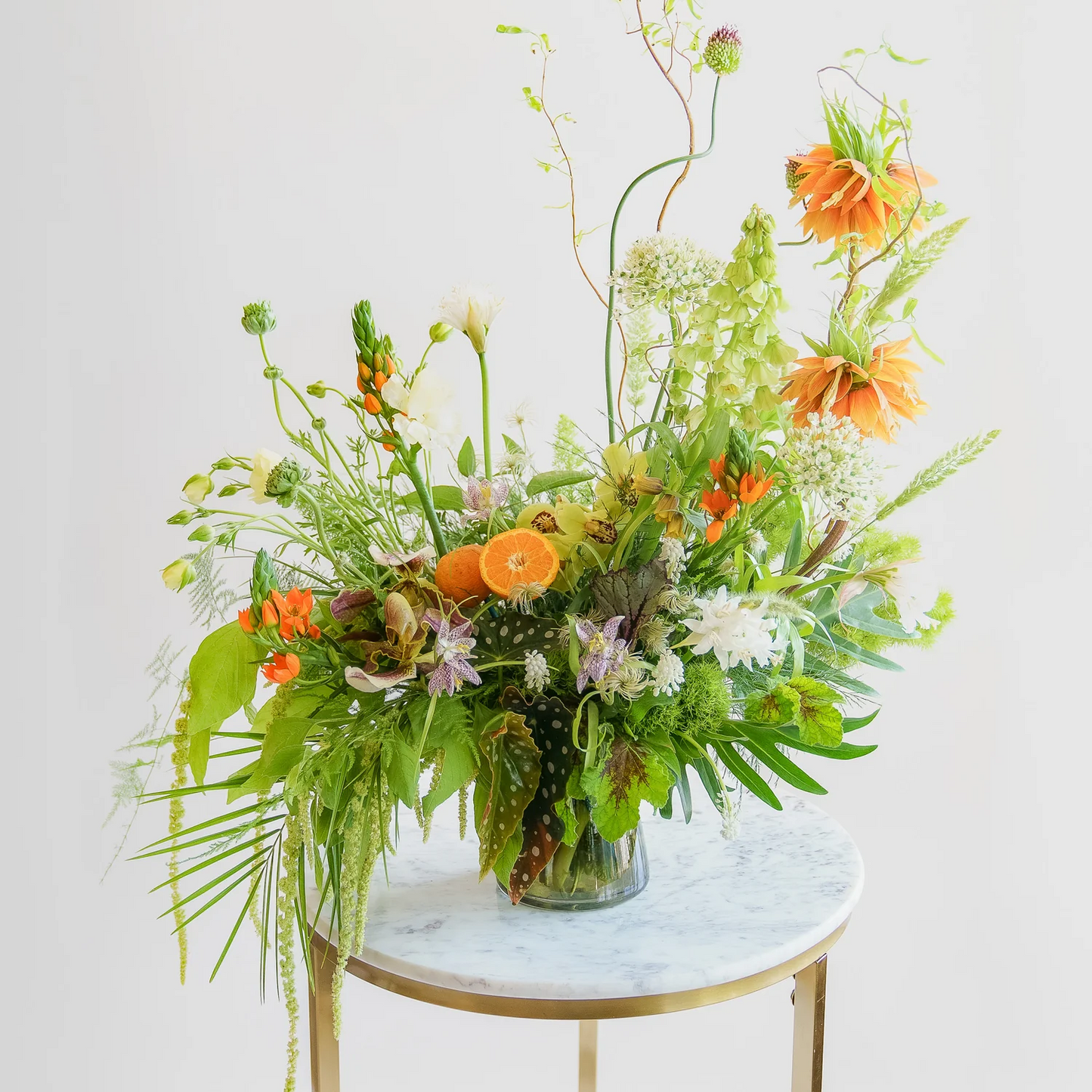 Floral arrangement with orange and green flowers on a marble table against a white background