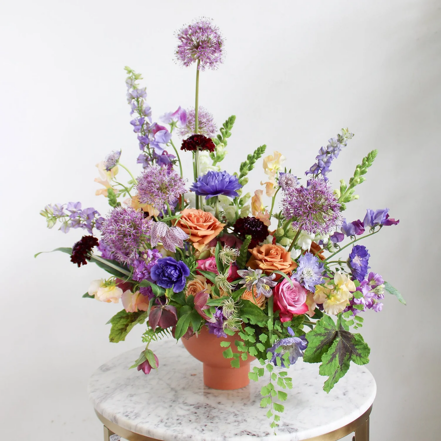 Colorful flower arrangement in a terracotta pot on a marble surface with a white background