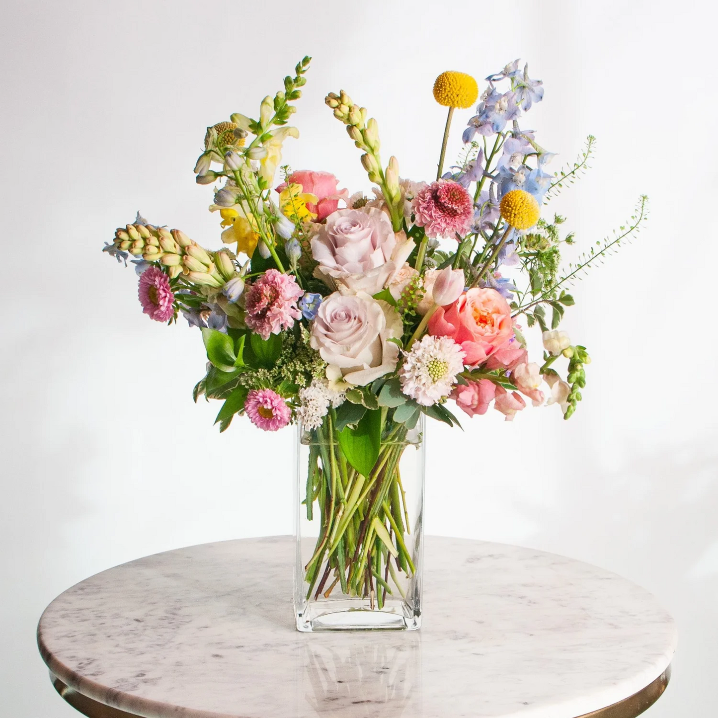 Bouquet of colorful flowers in a clear vase on a marble surface with a white background