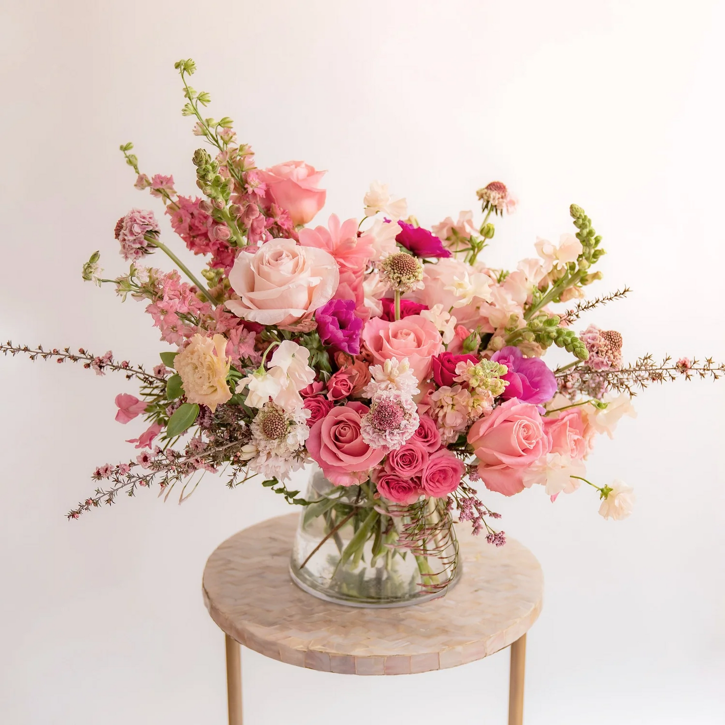 Bouquet of pink and white flowers in a clear vase on a small round wooden table with a light background