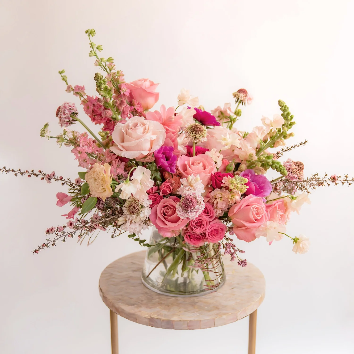 Bouquet of pink and white flowers in a clear vase on a small round wooden table with a light background
