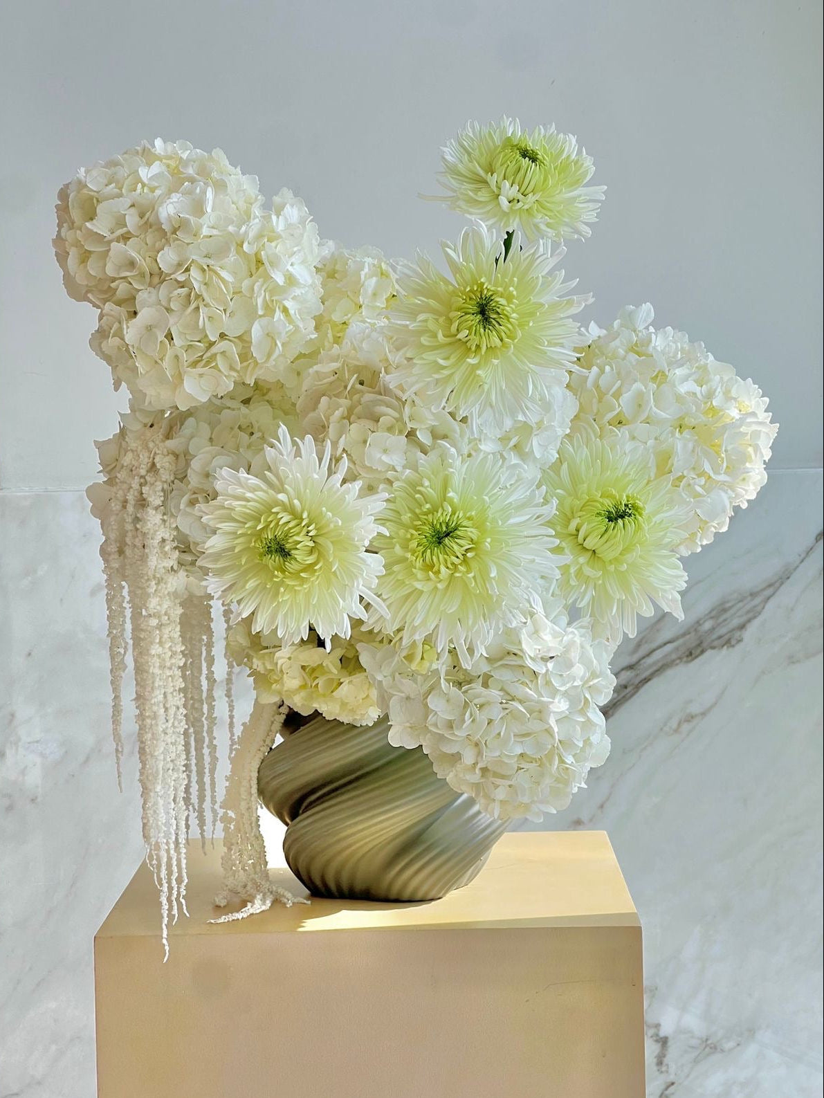 Decorative floral arrangement with white and light green flowers in a vase on a beige pedestal.