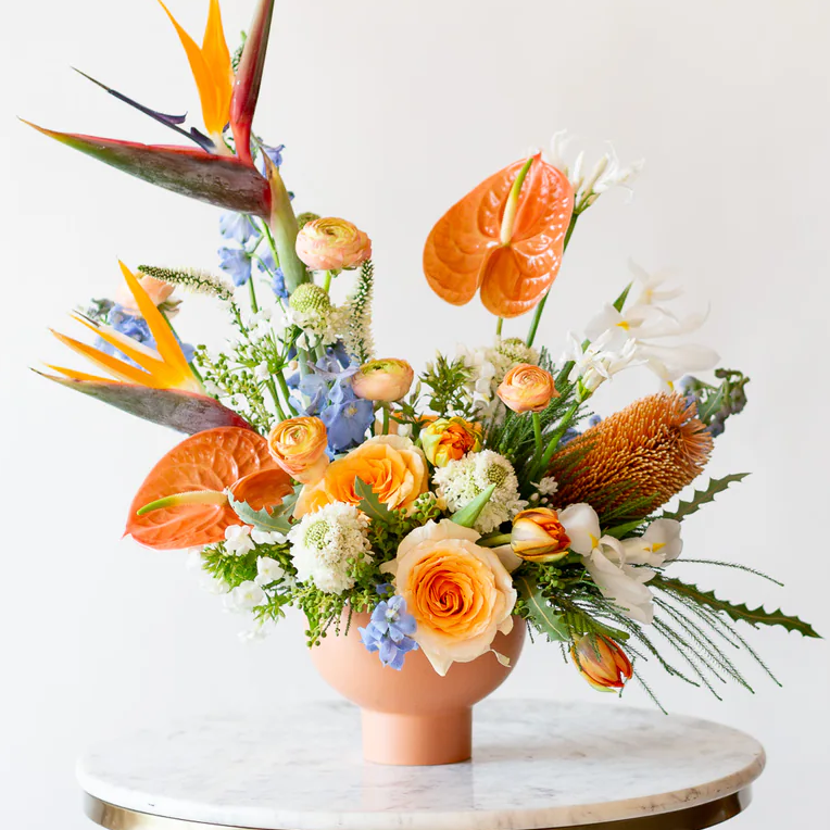 Colorful floral arrangement with tropical elements on a marble table against a white background