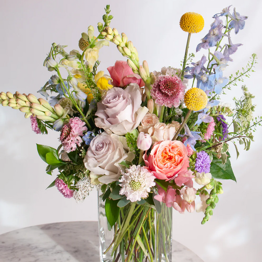 Colorful flower arrangement in a clear vase on a marble surface with a light gray background