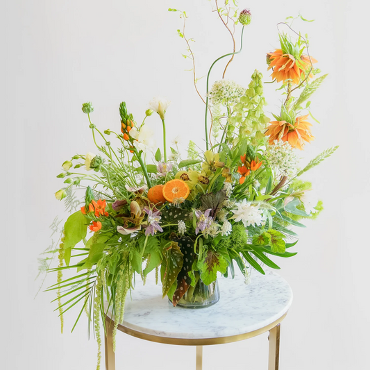 Floral arrangement with orange and green flowers on a marble table against a white background