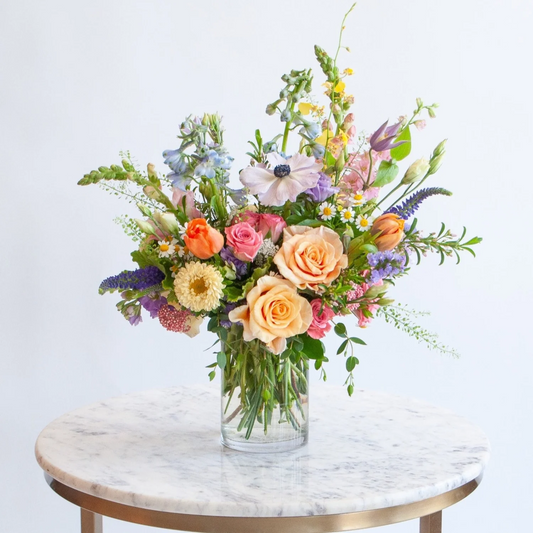 Bouquet of colorful flowers in a clear vase on a marble table with a white background