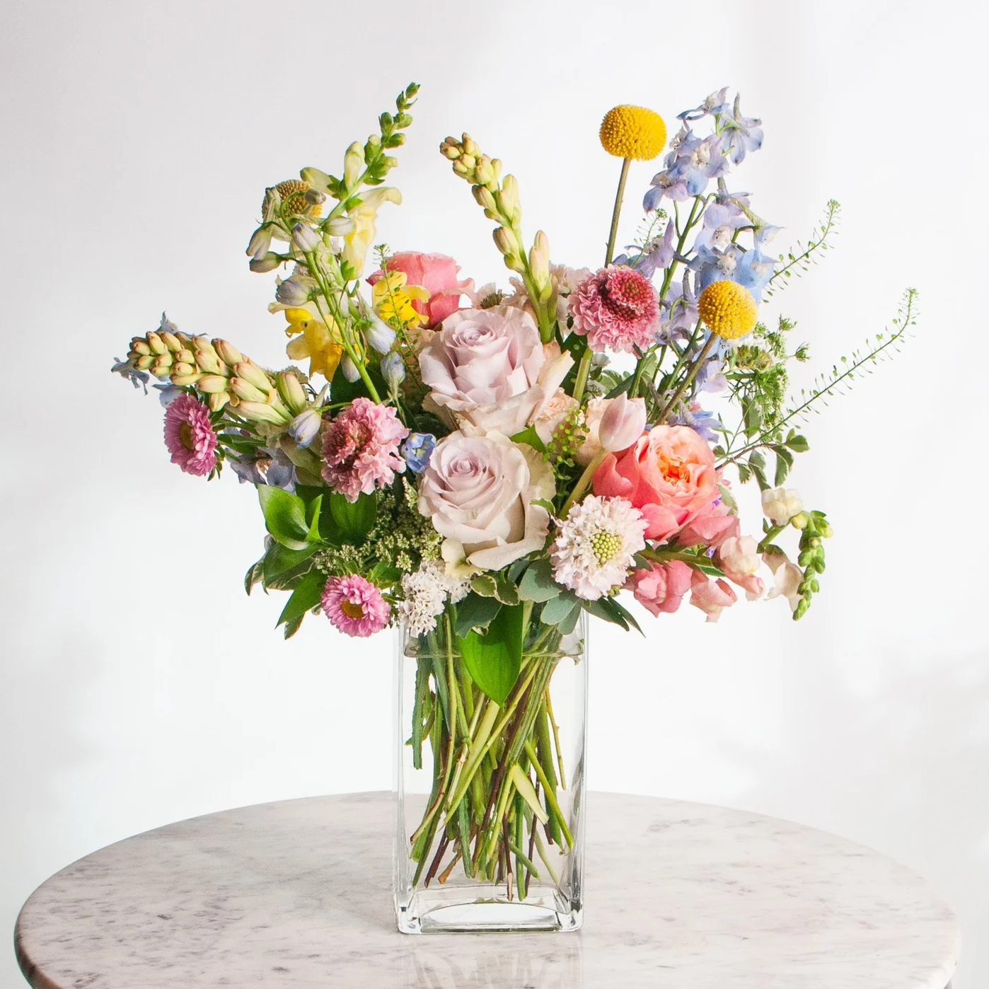 Bouquet of colorful flowers in a clear vase on a marble surface with a white background