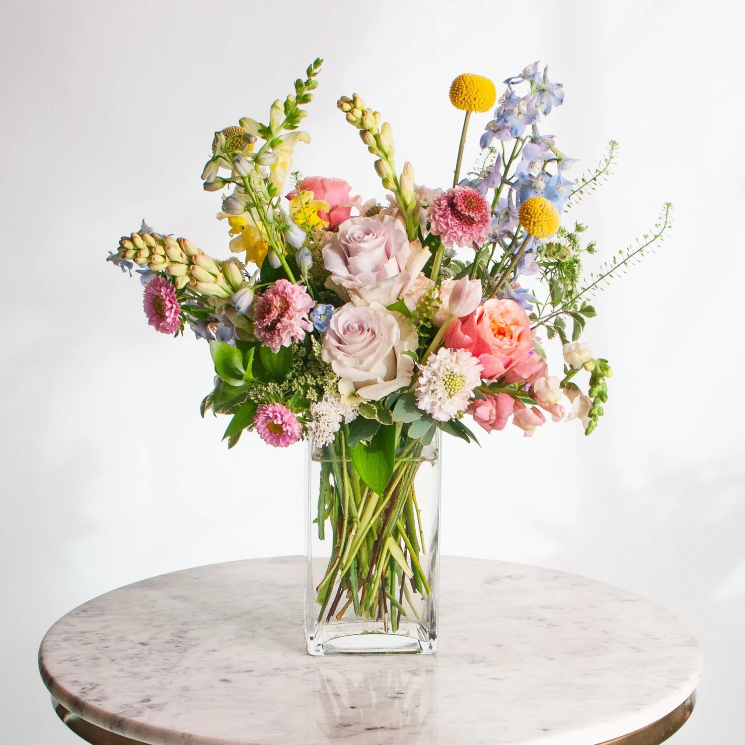 Bouquet of colorful flowers in a clear vase on a marble surface with a white background