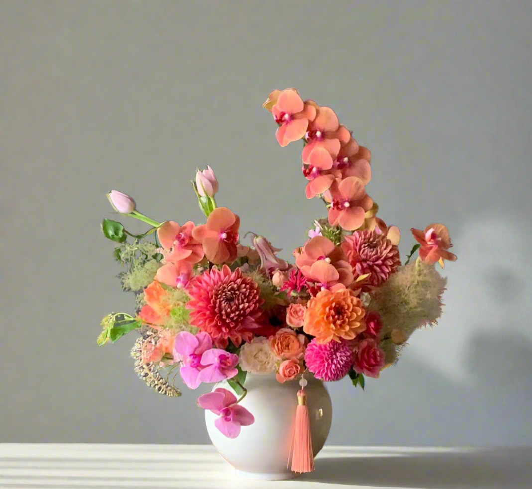 Floral arrangement in a white vase on a small wooden table against a gray wall.