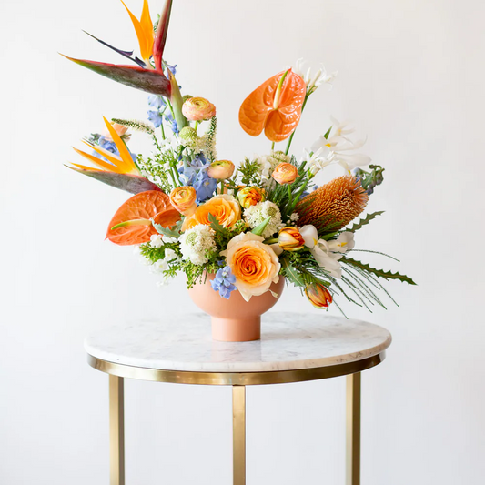 Colorful floral arrangement with tropical elements on a marble table against a white background